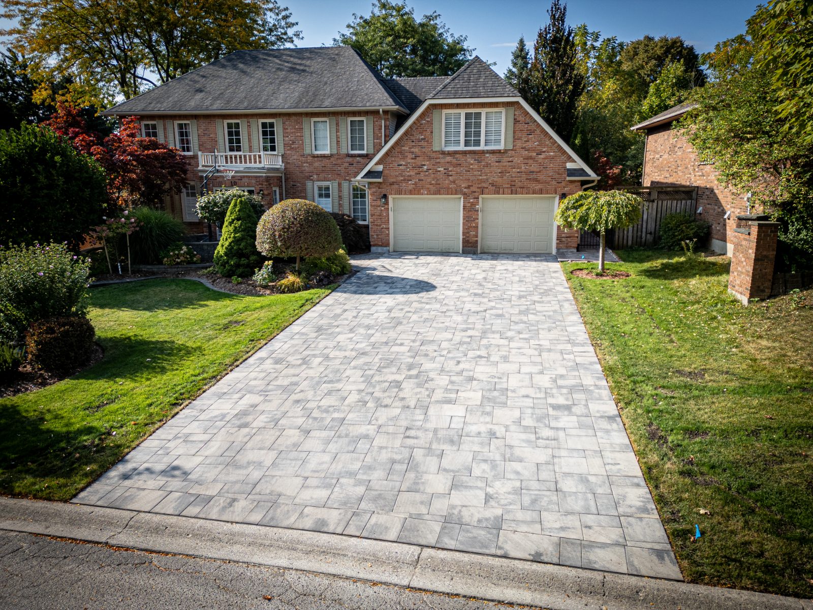 Completed residential interlocking paver driveway installation in front of a two-storey brick home